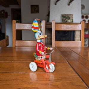 Vintage tin wind-up duck toy riding tricycle with colorful outfit and propeller hat for collector of mechanical toys