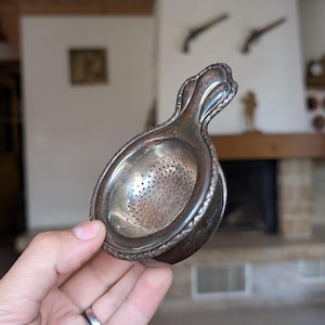 Sigg vintage metal tea strainer with sculpted handle and built-in bowl for traditional loose leaf brewing or rustic tea service