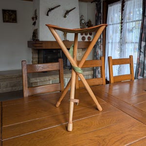 Banco dobrável suíço vintage com tripé, assento de lona verde e acabamento em couro para camping, caça ou decoração rústica