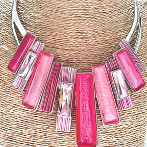May include: A silver and pink statement necklace with a geometric design. The necklace features multiple rectangular pieces of pink glass with a silver metal frame.
