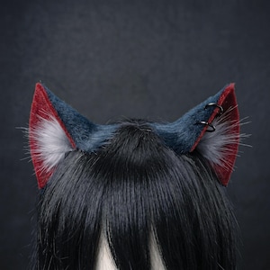 May include: A pair of faux fur cat ears in shades of navy blue, burgundy, and gray, with black hoop accents. The ears are attached to a black headband, creating a cosplay accessory.