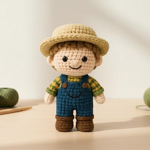 May include: A crocheted doll of a farmer wearing a tan hat, a yellow and green plaid shirt, and blue overalls. The doll has brown boots and a smiling face. Yarn and a crochet hook are on the table.
