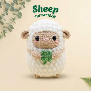 May include: A crocheted sheep with a white body, beige face, and small ears. The sheep holds a green four-leaf clover and has pink cheeks. The text "Sheep PDF Pattern" is above the sheep in green.