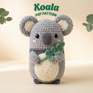 Peut inclure: Un koala au crochet gris fait à la main tenant une branche de feuilles vertes. Le koala a un ventre blanc, des oreilles intérieures et une rayure gris foncé. Le texte "Koala PDF Pattern" est en haut en vert.