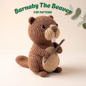 May include: A crocheted beaver toy named Barnaby The Beaver, featuring a brown body, a light tan belly, a dark brown nose, and two white teeth. The beaver is holding a small wooden stick. The text Barnaby The Beaver PDF PATTERN is visible.