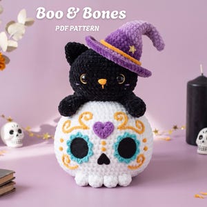 Puede incluir: Un patrón de ganchillo titulado Boo & Bones PDF Pattern que muestra un peluche de gato negro con un sombrero de bruja morado y una estrella dorada, sentado sobre una calavera blanca con cuencas azules, un corazón morado y detalles naranjas.