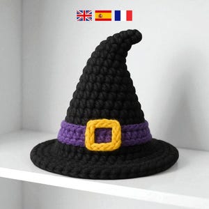 Könnte beinhalten: Ein schwarzer gehäkelter Hexenhut mit einem lila Band und einer gelben Schnalle. Der Hut hat eine breite Krempe und eine hohe, spitze Krone. Dieser Hut zum Thema Halloween ist perfekt für Kostüme und Dekorationen.