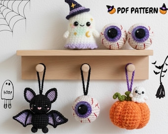 May include: A collection of handmade crochet Halloween decorations. Includes a ghost, two eyeball ornaments, a bat, a pumpkin with a ghost, and a single eyeball ornament. The decorations are displayed on a wooden shelf and hooks.