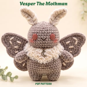 Può includere: Un peluche all'uncinetto chiamato Vesper The Mothman, con corpo grigio, grandi orecchie soffici, colletto in pelliccia sintetica color crema, occhi circolari rosso scuro, guance rosa e ali con cuciture chiare. Un ciondolo a mezzaluna argentato pende dal collo.