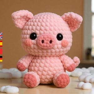May include: A handmade pink crochet pig with black eyes, a pink snout, and blush-colored cheeks. The pig has small ears, arms, and legs. The plush toy is sitting on a wooden surface.
