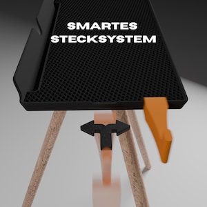 Peut inclure: Un plateau rectangulaire noir avec une surface alv&eacute;ol&eacute;e textur&eacute;e et le texte blanc SMARTES STECKSYSTEM. Le plateau comporte un crochet orange sur le c&ocirc;t&eacute; et est soutenu par des pieds en bois clair avec un connecteur noir en forme de T.