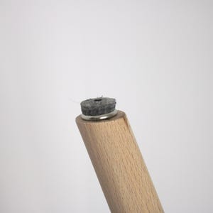 Peut inclure: Un pied de meuble en bois clair dot&eacute; d'une base m&eacute;tallique circulaire fix&eacute;e &agrave; l'extr&eacute;mit&eacute;. Un patin en feutre gris fonc&eacute;, &eacute;pais et circulaire, est fix&eacute; sur la base m&eacute;tallique pour prot&eacute;ger les surfaces des rayures et des &eacute;raflures.