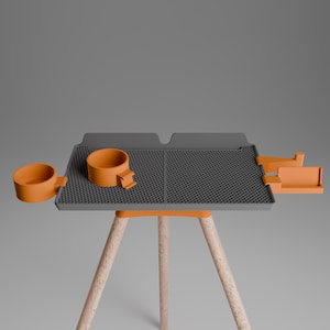 Peut inclure: Un plateau rectangulaire gris &agrave; surface quadrill&eacute;e textur&eacute;e, soutenu par trois pieds en bois clair. Le plateau comporte des accessoires orange, dont deux porte-gobelets circulaires sur le c&ocirc;t&eacute; gauche et un compartiment de rangement rectangulaire &agrave; droite.