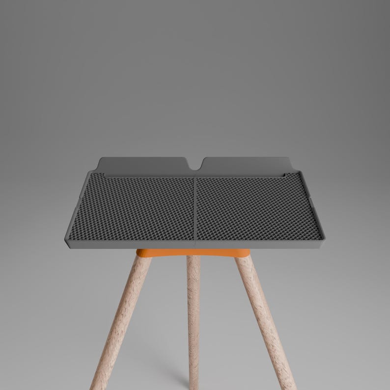 Peut inclure: Un tapis de s&eacute;chage rectangulaire en silicone gris fonc&eacute; avec une surface &agrave; grille textur&eacute;e et un bord sur&eacute;lev&eacute;, soutenu par un cadre orange et trois pieds en bois clair. Le tapis pr&eacute;sente une s&eacute;paration centrale et deux sections distinctes.