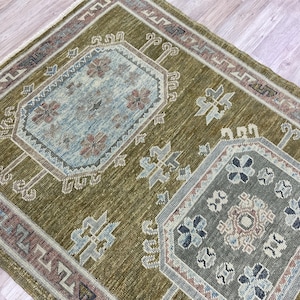 May include: A rectangular area rug featuring an olive green background with two central octagonal medallions in shades of light blue and grey. The rug includes intricate geometric patterns, floral motifs, and a decorative border in muted tones.