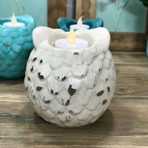 Puede incluir: Portavelas de cer&aacute;mica blanca en forma de b&uacute;ho con un acabado desgastado. El b&uacute;ho tiene un cuerpo redondo con una superficie texturizada y una peque&ntilde;a abertura en la parte superior para una vela de t&eacute;.