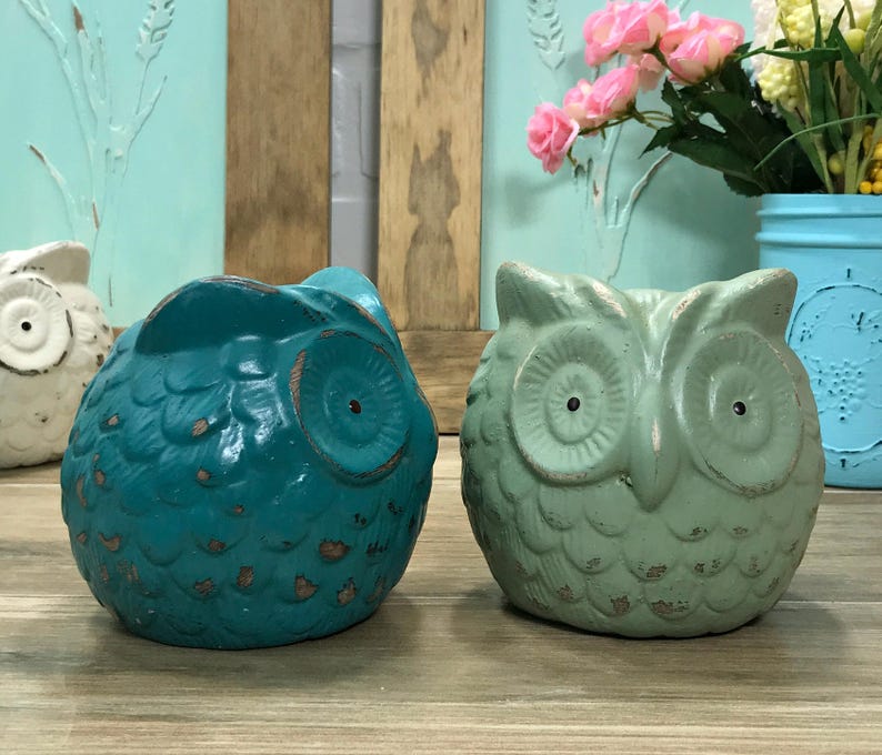 Puede incluir: Dos figuritas de b&uacute;ho de cer&aacute;mica, una azul verdosa y otra verde claro, con detalles texturizados y ojos pintados.