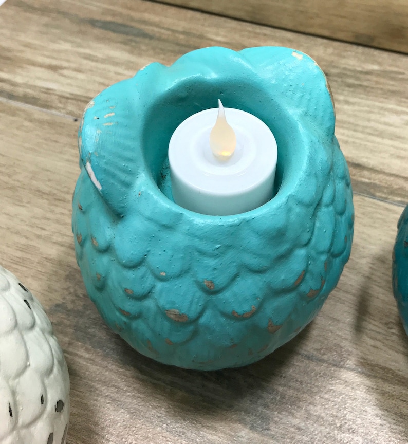 Puede incluir: Portavelas de cer&aacute;mica azul turquesa en forma de b&uacute;ho con una vela de t&eacute; blanca en su interior. El b&uacute;ho tiene una superficie texturizada que se asemeja a escamas.