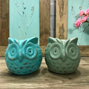 Puede incluir: Dos figuritas de b&uacute;ho de cer&aacute;mica azul verdoso con pintura desgastada. Los b&uacute;hos tienen ojos grandes y un dise&ntilde;o detallado.
