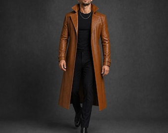 May include: A long tan leather trench coat with a wide collar and belted cuffs, worn over a black crew neck t-shirt and black trousers. The coat features a structured silhouette, long sleeves, and a smooth finish, paired with black leather boots.
