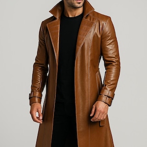 Pode incluir: Um casaco comprido de couro castanho com um design clássico de trench coat. O casaco apresenta uma gola larga, uma frente de abotoamento duplo e um cinto na cintura. As mangas têm detalhes de fivelas nos punhos. O casaco é até ao joelho.