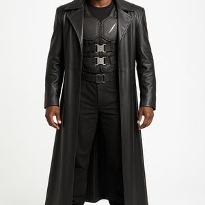 May include: A full-length image of a person wearing a black leather trench coat, a black vest with silver accents, black pants, and black boots. The person is also wearing black sunglasses.