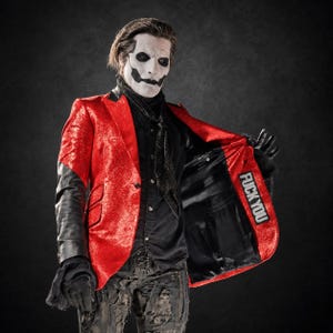 May include: A bright red glitter blazer with black leather sleeves and a black shirt underneath. The interior lining of the blazer features a rectangular patch with the text FUCK YOU printed in white capital letters on a black background.