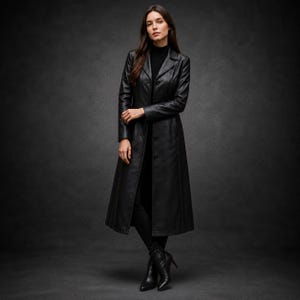 May include: A long black leather coat featuring a structured collar, long sleeves, and a button-front closure. The coat is worn over a black turtleneck top, black trousers, and black pointed-toe ankle boots, creating a monochromatic ensemble.
