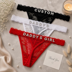 May include: Three thong panties in black, white, and red lace, each featuring a scalloped waistband with rhinestone lettering. The black pair reads CUSTOM, the white pair reads DADDYS, and the red pair reads DADDYS GIRL in silver-toned crystals.