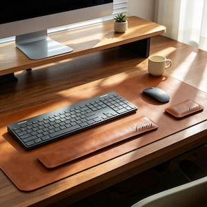 Peut inclure: Un ensemble de sous-main en cuir beige comprenant un repose-poignet rectangulaire pour clavier et un plus petit pour souris, tous deux gravés du nom Lonny. L'ensemble inclut un clavier sans fil gris foncé et une souris assortie.