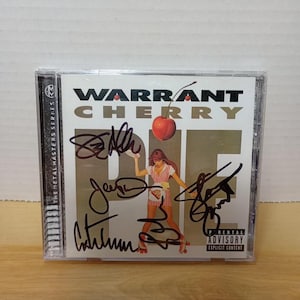 May include: A Warrant "Cherry Pie" CD in a clear plastic case. The album cover features the band's name and album title, with a woman holding a pie. The CD case is signed by the band members. Parental Advisory Explicit Content warning is visible.