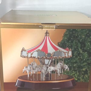 May include: Musical carousel with a red and white striped canopy and gold trim. The carousel features white horses and is displayed in a box with the Dillard's logo. The text "MUSICAL CAROUSEL" is visible on the box.