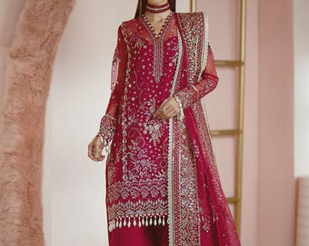 May include: A formal, ruby red ensemble featuring intricate silver embroidery. The outfit includes a long-sleeved tunic, wide-leg pants, and a matching sheer scarf. The design is embellished with delicate beadwork and a scalloped hem.