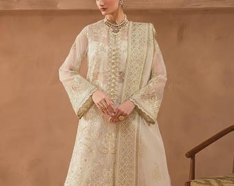 May include: Off-white embroidered formal wear ensemble. The outfit includes a long-sleeved tunic, matching pants, and a sheer scarf. The tunic features intricate gold embroidery and embellishments. The outfit is worn with gold heels and jewelry.