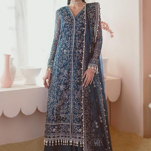 Op de afbeelding: Een lange, donkerblauwe jurk met ingewikkelde bloemenborduurwerk en een bijpassende doorschijnende sjaal. De jurk heeft een V-hals, lange mouwen en delicate kralen langs de randen. De set is elegant en geschikt voor formele gelegenheden.
