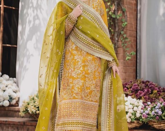 May include: Mustard yellow embroidered salwar kameez with a matching dupatta. The outfit features intricate gold embroidery and a patterned border. The dupatta is a sheer, olive green fabric with gold trim. The ensemble is a traditional South Asian style.