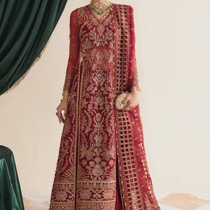May include: A formal red embroidered gown with gold accents. The long-sleeved dress features intricate floral patterns and a matching shawl. The outfit includes a gold clutch and jewelry, creating an elegant ensemble.