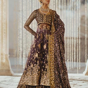 May include: A formal, dark purple and gold embroidered gown with a matching shawl. The long-sleeved top and full skirt are heavily embellished with gold floral patterns. The shawl is draped over the shoulder, and the model is wearing gold jewelry.