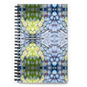 May include: Spiral-bound notebook with a vibrant abstract design. The cover displays a symmetrical pattern of green, yellow, blue, and purple brushstrokes. The notebook has a black spiral binding.