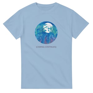 May include: Light blue t-shirt featuring a circular graphic with a forest and moon design in shades of blue and green. The text "[CAWING CONTINUES]" is printed below the graphic. The shirt is made of a soft material.