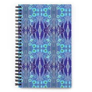 May include: A spiral-bound notebook with a blue floral design. The cover features a symmetrical pattern of stylized flowers and leaves in shades of blue, teal, and purple. The notebook's spiral binding is black.