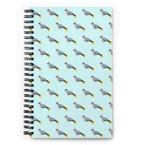 May include: Spiral-bound notebook with a repeating pattern of stylized birds on a light blue background. The birds have grey bodies, yellow tail feathers, and red accents. The notebook's spiral binding is black.