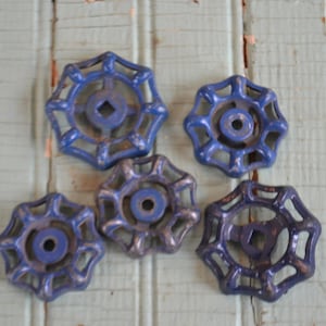 Puede incluir: Cinco manijas de grifo de agua azules vintage con un diseño de estrella. Las manijas son de metal y muestran signos de desgaste, con algunas astillas de pintura. Las manijas están dispuestas sobre una superficie de madera azul claro desgastada.
