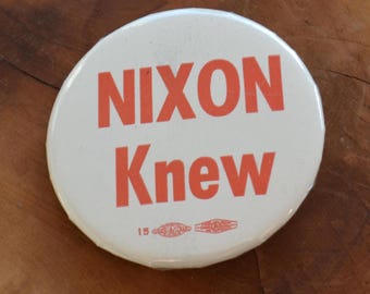May include: A white button with the text "Nixon Knew" in red letters. The button has a small number "15" printed on the bottom.