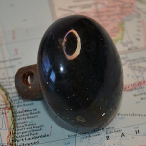 Peut inclure: Un bouton de porte en verre bleu foncé avec un anneau blanc autour du centre. Le bouton est fixé à une tige métallique rouillée.