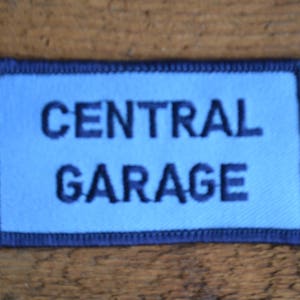 May include: A blue and black embroidered patch with the text "CENTRAL GARAGE" in white.