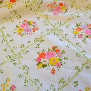 May include: White fabric with a repeating pattern of floral bouquets and green vines. The bouquets feature pink, yellow, orange, and purple flowers. The vines form a diamond grid across the fabric.