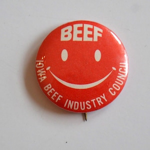 Puede incluir: Botón rojo con una cara sonriente blanca y el texto "BEEF" en la parte superior. El texto "IOWA BEEF INDUSTRY COUNCIL" rodea la cara sonriente.