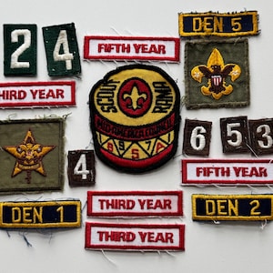 May include: A collection of colorful embroidered patches featuring the words "Den 5", "Fifth Year", "Third Year", "Den 1", "Den 2", "6", "5", "3", and "Scout Rama", along with a yellow and red patch with a scout emblem.