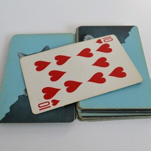 May include: A playing card with a ten of hearts design. The card is lying on top of a stack of cards with a blue background and a picture of a cat.